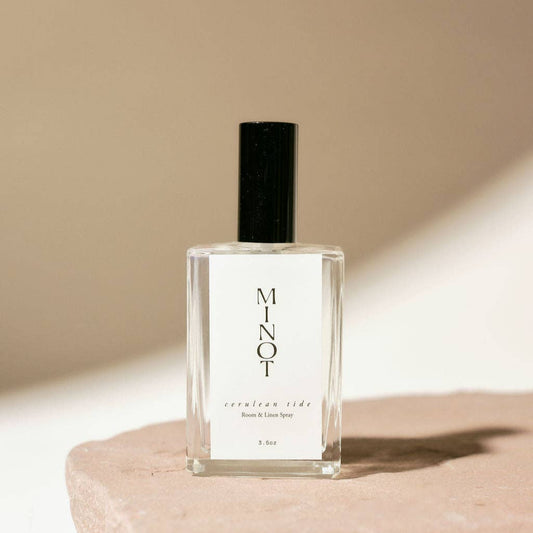 A small clear bottle with a black spray nozzle, labeled 'Cerulean Tide Room & Linen Spray' with a white cap, presented on a beige background.